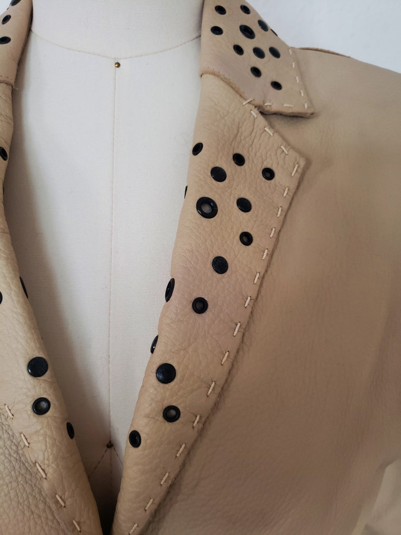 Detail view of 1990s topstitched metal eyelet and stud embellished buff leather blazer by Donald Pliner, extra small to small, showing the topstitched collar embellished with black eyelets and studs.