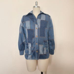 May include: A blue long-sleeved shirt with a geometric patchwork design. The shirt has a button-up front and two pockets.