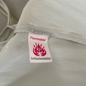 Interior detail view of 2000s y2k vintage new with tags sage green silk charmeuse robe by Patricia Fieldwalker, size medium to large. Showing the flammable tag.