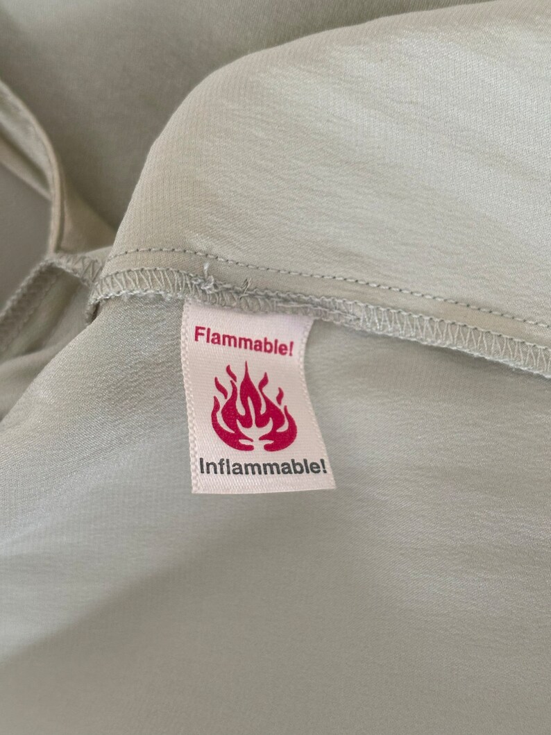 Interior detail view of 2000s y2k vintage new with tags sage green silk charmeuse robe by Patricia Fieldwalker, size medium to large. Showing the flammable tag.