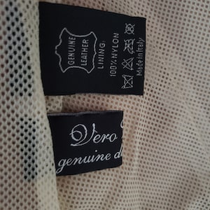 Detail view of 1990s topstitched metal eyelet and stud embellished buff leather blazer by Donald Pliner, extra small to small, showing the mesh lining and fabric content tags.