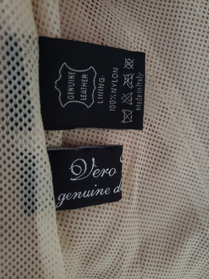 Detail view of 1990s topstitched metal eyelet and stud embellished buff leather blazer by Donald Pliner, extra small to small, showing the mesh lining and fabric content tags.