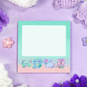 Può includere: Un blocco note quadrato con un motivo a griglia verde chiaro e un bordo rosa. La parte inferiore del blocco note presenta quattro piccole illustrazioni di una cassetta, una rana, un floppy disk e una fotocamera. Lo sfondo è lilla chiaro.