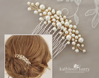 Puede incluir: Un peine para el cabello de oro y perlas blancas con un diseño delicado. El peine tiene una base plateada con una fila de dientes. Las perlas están dispuestas en un racimo y están rodeadas de alambre dorado.