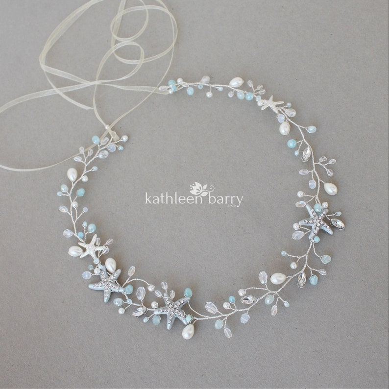 May include: A delicate silver bridal hair vine with blue and white beads, pearls, and starfish accents. The vine is tied with a sheer ribbon.