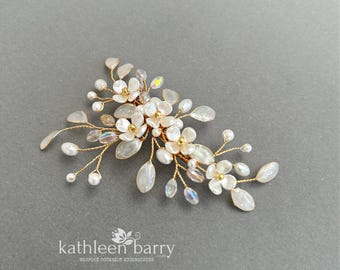 May include: A hair accessory featuring white floral shapes, small pearls, and iridescent crystal beads arranged on thin gold-toned wire branches. The text kathleen barry BESPOKE OCCASION ACCESSORIES is printed in white at the bottom of the image.