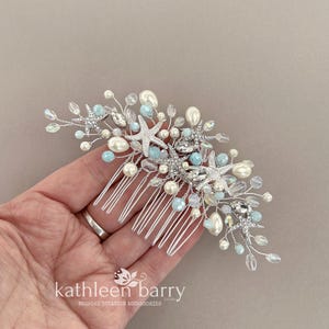 May include: A silver hair comb featuring a coastal design with multiple starfish accents, light blue beads, clear crystals, and white faux pearls arranged on thin silver wire branches. The text kathleen barry is printed at the bottom.