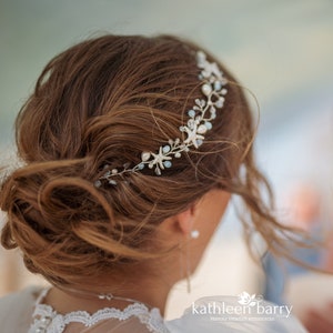 May include: A delicate hair comb with a silver wire base adorned with white and blue starfish, pearls, and crystals. The comb is worn in a woman's brown hair.