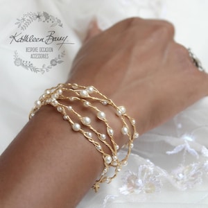 Puede incluir: Pulsera de alambre dorado con perlas blancas, con un diseño delicado e intrincado. La pulsera está hecha de varios hilos de alambre, cada uno adornado con pequeñas perlas. La pulsera es una pieza de joyería hermosa y elegante que sería perfecta para una ocasión especial.