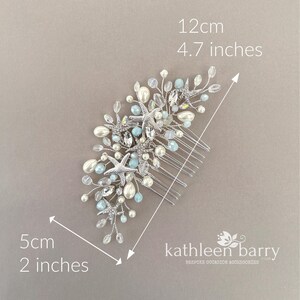 May include: A silver hair comb featuring starfish, white pearls, and light blue beads on wire branches. The accessory measures 12 cm by 5 cm, or 4.7 inches by 2 inches. The text "kathleen barry" is printed in the bottom right corner.