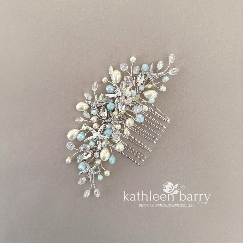 May include: A silver hair comb featuring a coastal design with metallic starfish, white faux pearls, and light blue crystal beads arranged on flexible wire branches. The accessory includes the text kathleen barry BESPOKE OCCASION ACCESSORIES.