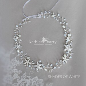 May include: A silver and white starfish hair comb with pearls and crystals. The comb is in the shape of a circle and is decorated with starfish, pearls, and crystals. The comb is on a grey background.  Kathleen Barry Bespoke Occasion Accessories.