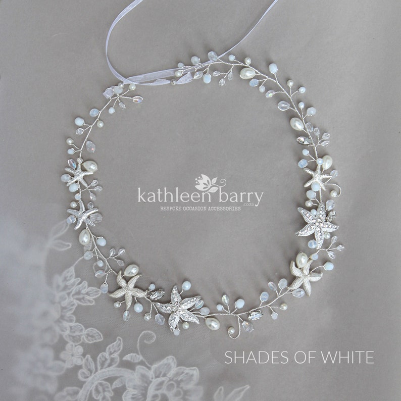 May include: A silver and white starfish hair comb with pearls and crystals. The comb is in the shape of a circle and is decorated with starfish, pearls, and crystals. The comb is on a grey background.  Kathleen Barry Bespoke Occasion Accessories.