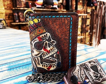 May include: A brown leather wallet with a skull and Native American headdress design. The wallet has a chain attached to it and a matching key chain with a skull design.