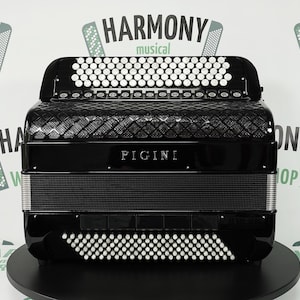 May include: A black accordion with white button keys and a diamond pattern on the top. The brand name "PIGINI" is visible. The accordion is on a black surface. The background has the words "HARMONY musical WORKSHOP".