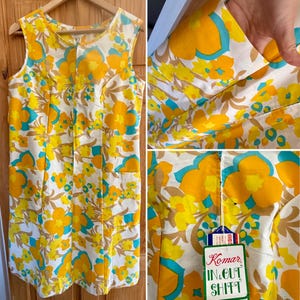 May include: A vintage shift dress with a bright floral pattern in yellow, orange, and turquoise on a white background. The sleeveless dress has a round neckline, two front pockets, and a zip. The tag reads "Komar IN & OUT SHIFT".