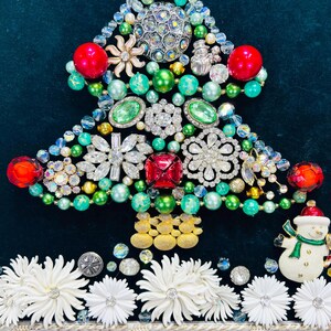 May include: A Christmas tree crafted from green, red and white beads, rhinestones and jewellery. The tree is adorned with a snowman ornament and white flowers at the base.