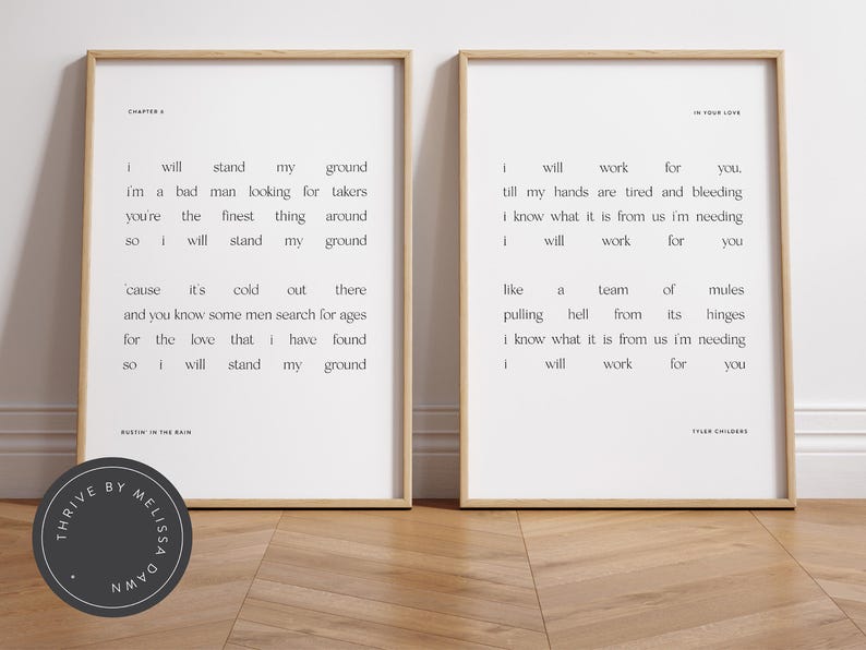 May include: Two framed art prints with minimalist text on a white background. One print reads "Chapter 6" and the other "In Your Love." The prints are in wooden frames and are displayed on a wooden floor.