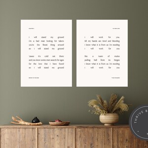 May include: Two framed art prints with minimalist typography on a neutral background. The prints feature song lyrics in a simple, elegant font. The artwork is displayed on a wooden cabinet with decorative items, creating a warm, inviting aesthetic.