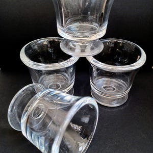 May include: Clear glass shot glasses with a flared top and a thick base. One glass is upside down, and the others are stacked. The glasses are on a black surface.