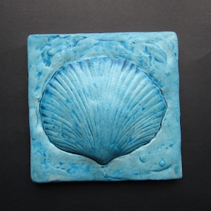 May include: A blue ceramic tile with a raised seashell design. The tile has a textured surface and a light blue color.