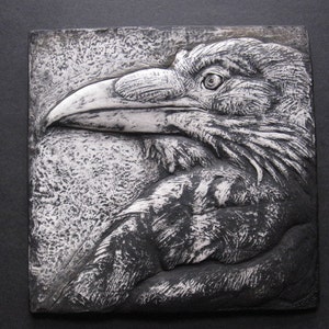May include: A black and white ceramic wall sculpture of a raven's head with a detailed, textured surface.