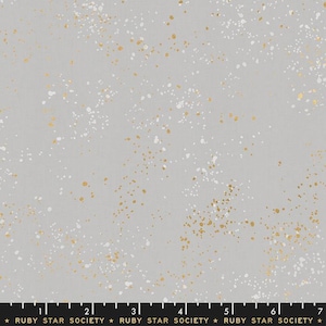 May include: A light gray fabric with a speckled pattern of white and gold metallic paint splatters. The fabric has a subtle texture and is suitable for quilting or other craft projects. The text "RUBY STAR SOCIETY" is printed at the bottom.