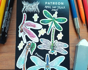 May include: A black sticker sheet with dragonfly designs in shades of pink, green, and blue. The sheet is labelled "PATREON APRIL 2025 STICKER SHEET" and includes the artist's handle, "@PHASEMOTH".