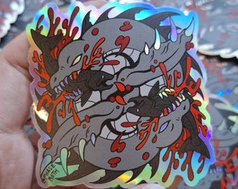 May include: A holographic sticker featuring a circular illustration of two grey, sharp-toothed fish swimming in a yin-yang formation, surrounded by bright red coral-like shapes. The text "PHASE MOTH" is printed in the bottom left corner.