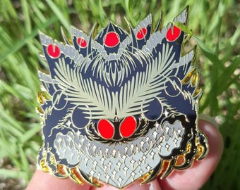 May include: A metal enamel pin featuring a stylized moth design with a dark navy blue body, light gray fur-like details, and bright red circular accents. The design includes intricate wing patterns and a textured lower section with star shapes.