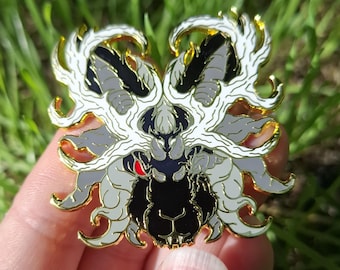 May include: A metal enamel pin featuring a stylized creature head with black fur, grey accents, and a single bright red eye. The design includes intricate white flame-like patterns surrounding the head, all outlined in a polished gold-tone metal finish.