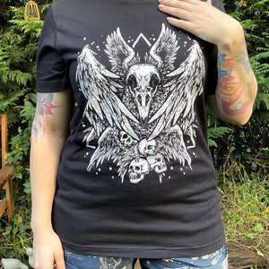 Peut inclure: T-shirt noir avec un imprim&eacute; blanc d'un cr&acirc;ne avec des ailes et des cha&icirc;nes. Le cr&acirc;ne est entour&eacute; d'un motif g&eacute;om&eacute;trique et de petits points blancs.
