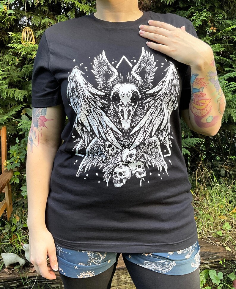Peut inclure: T-shirt noir avec un imprim&eacute; blanc d'un cr&acirc;ne avec des ailes et des cha&icirc;nes. Le cr&acirc;ne est entour&eacute; d'un motif g&eacute;om&eacute;trique et de petits points blancs.