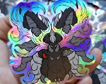 May include: A holographic sticker featuring a stylised black creature head with multiple eyes, sharp fangs, and flowing, flame-like hair in shades of blue, purple, and yellow. The text "PHASE MOTH" is printed in small black letters on the right side.