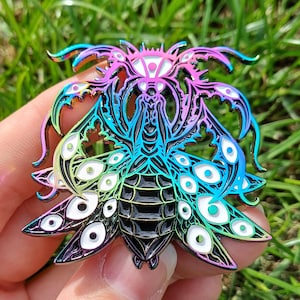 May include: An iridescent insect pin with a detailed design. The pin features a stylized insect with multiple eye-like shapes and a gradient of colours, including blue, pink, and green. The pin is made of metal and has a glossy finish.