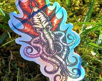 May include: A holographic sticker featuring a detailed illustration of a Cthulhu-like creature with tentacles and a menacing expression. The creature is depicted with a red and black colour scheme, and the sticker has a holographic finish that shimmers in different colours.
