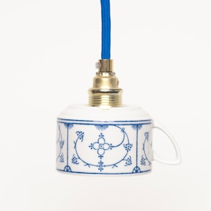 May include: A white porcelain pendant light with a blue and white floral design. The light has a gold-colored socket and a blue cord.