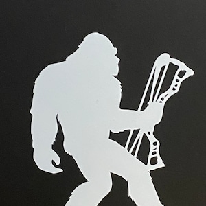 Puede incluir: Silueta blanca de un Bigfoot sosteniendo un arco y una flecha. El Bigfoot camina hacia adelante con el pie derecho delante del izquierdo. El arco y la flecha se sostienen en su mano derecha.