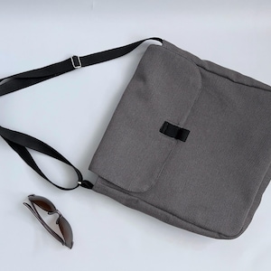 Peut inclure: Un sac messager en toile grise avec une bandoulière noire réglable. Le sac a une fermeture à rabat avec une boucle noire.