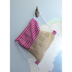 Peut inclure: Un sac en tissu à rayures roses et blanches avec un fond en toile de jute brune. Le sac est suspendu à un crochet en forme de tête de renard.