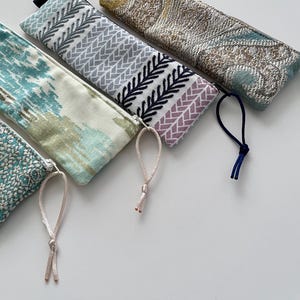 Peut inclure: Quatre trousses rectangulaires à fermeture éclair avec des motifs en tissu distincts. L'une présente un imprimé abstrait bleu sarcelle et blanc, une autre un motif chevron géométrique violet et noir, et deux arborent des motifs cachemire.