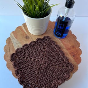 K&ouml;nnte beinhalten: Ein braunes geh&auml;keltes Geschirrtuch mit einem gewellten Rand liegt auf einem Holztablett mit einer durchsichtigen Glasflasche Sp&uuml;lmittel mit der Aufschrift "DISHES" und einer Topfpflanze.