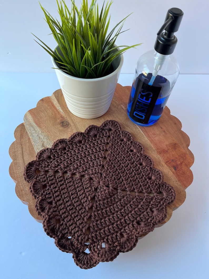K&ouml;nnte beinhalten: Ein braunes geh&auml;keltes Geschirrtuch mit einem gewellten Rand liegt auf einem Holztablett mit einer durchsichtigen Glasflasche Sp&uuml;lmittel mit der Aufschrift "DISHES" und einer Topfpflanze.