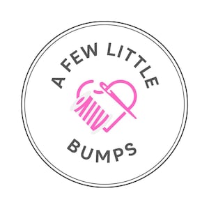 K&ouml;nnte beinhalten: Ein wei&szlig;er Kreis mit grauer Umrandung enth&auml;lt den Text "A FEW LITTLE BUMPS" in Schwarz. Im Inneren des Kreises befindet sich ein rosa Herz mit wei&szlig;em Rand. Das Herz enth&auml;lt ein stilisiertes Bild einer Garnrolle und einer Nadel.