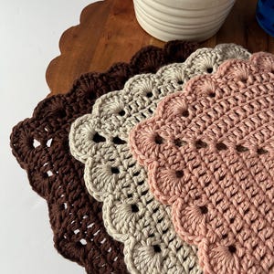 K&ouml;nnte beinhalten: Drei geh&auml;kelte Tischsets in Braun, Beige und Rosa mit gewellten R&auml;ndern.