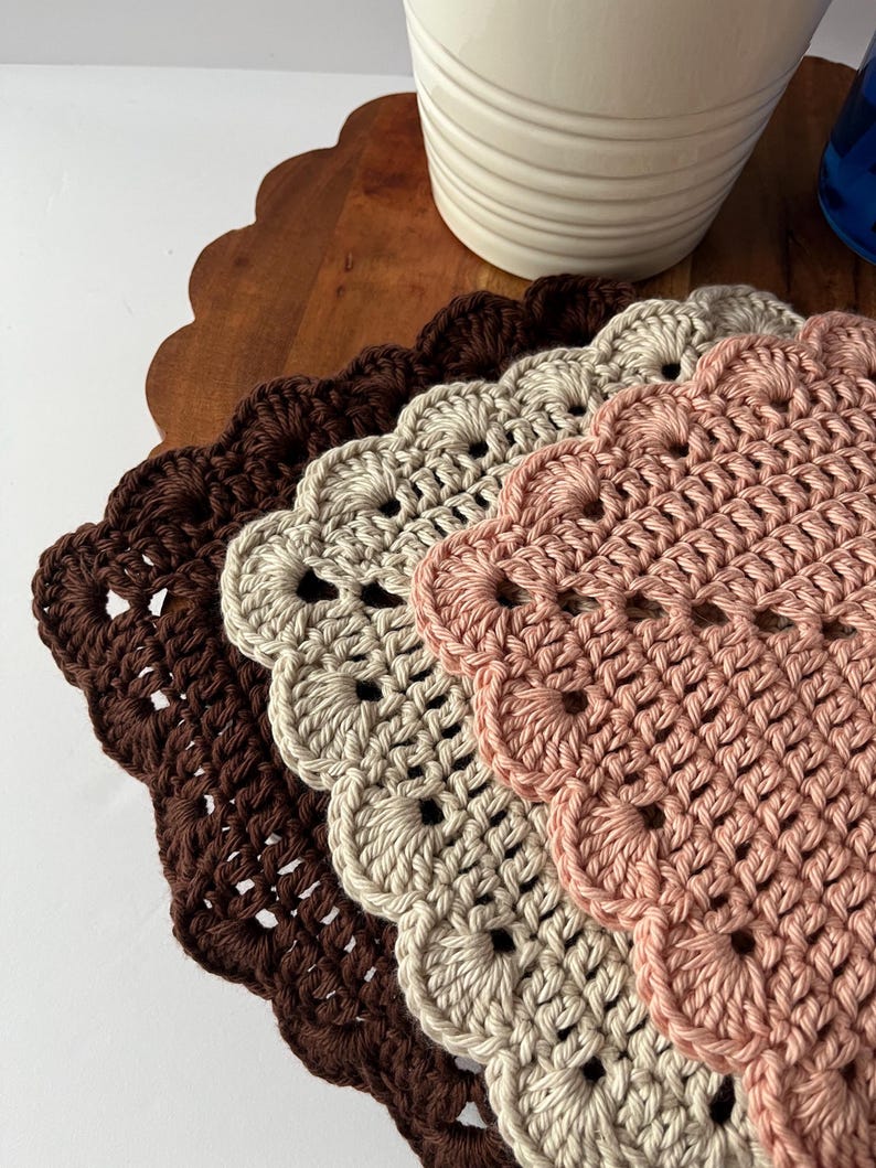K&ouml;nnte beinhalten: Drei geh&auml;kelte Tischsets in Braun, Beige und Rosa mit gewellten R&auml;ndern.