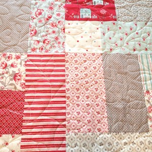 Peut inclure: Gros plan sur une courtepointe patchwork avec divers motifs et couleurs. La courtepointe pr&eacute;sente des carr&eacute;s avec des motifs floraux, ray&eacute;s et g&eacute;om&eacute;triques en rouge, blanc et gris. Certains carr&eacute;s ont des d&eacute;tails matelass&eacute;s.