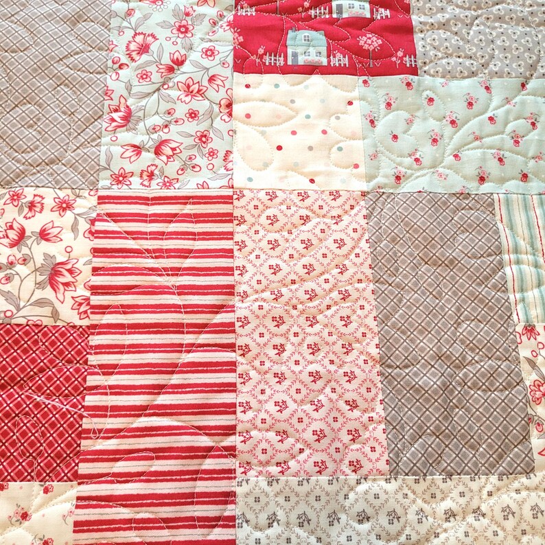Peut inclure: Gros plan sur une courtepointe patchwork avec divers motifs et couleurs. La courtepointe pr&eacute;sente des carr&eacute;s avec des motifs floraux, ray&eacute;s et g&eacute;om&eacute;triques en rouge, blanc et gris. Certains carr&eacute;s ont des d&eacute;tails matelass&eacute;s.