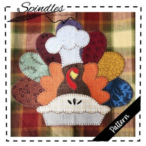 May include: A colorful Thanksgiving-themed fabric applique featuring a turkey wearing a chef's hat and a pie. The turkey's feathers are various patterned fabrics in shades of orange, brown, green, and blue. The pie crust is a light gray with decorative stitching.