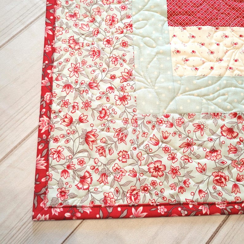 Peut inclure: Gros plan sur un textile matelass&eacute; &agrave; motifs floraux. La courtepointe pr&eacute;sente un tissu floral rouge et blanc, un tissu bleu clair &agrave; pois et une bordure rouge. La couture cr&eacute;e un effet textur&eacute;, mettant en valeur un artisanat fait &agrave; la main.